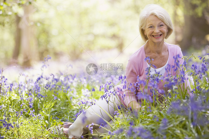 妇女坐在户外 鲜花微笑着女士享受野花退休采摘相机森林公园木头农村图片