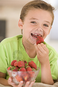 坐着草莓的男孩小男孩在客厅吃草莓时微笑着笑儿童享受饮食食品水果浆果家庭一个男孩食物孩子背景
