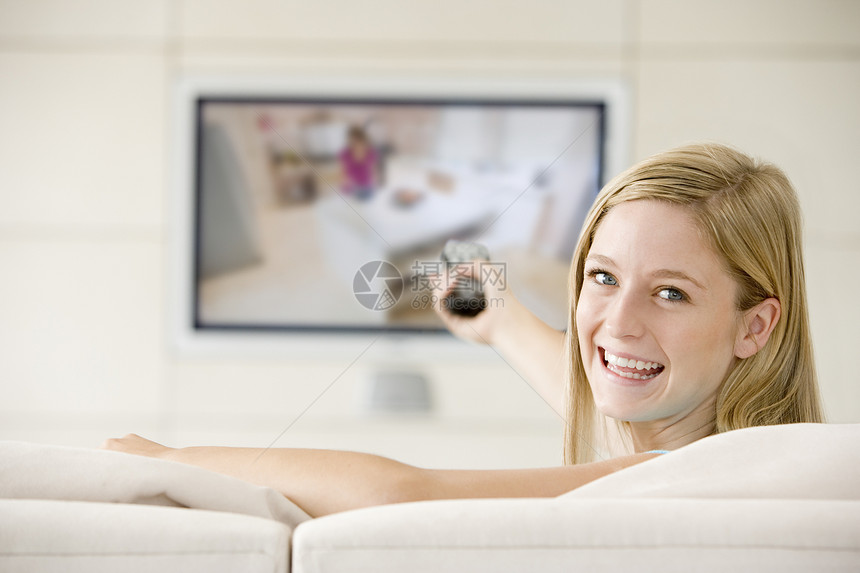 在客厅里看电视笑着的女子沙发遥控女性相机技术家庭纯平屏幕水平平面图片