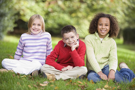 三名儿童坐在户外公园中微笑着笑容的小孩焦距孩子们成年人叶子家庭情感孩子情绪人种途径落叶高清图片素材