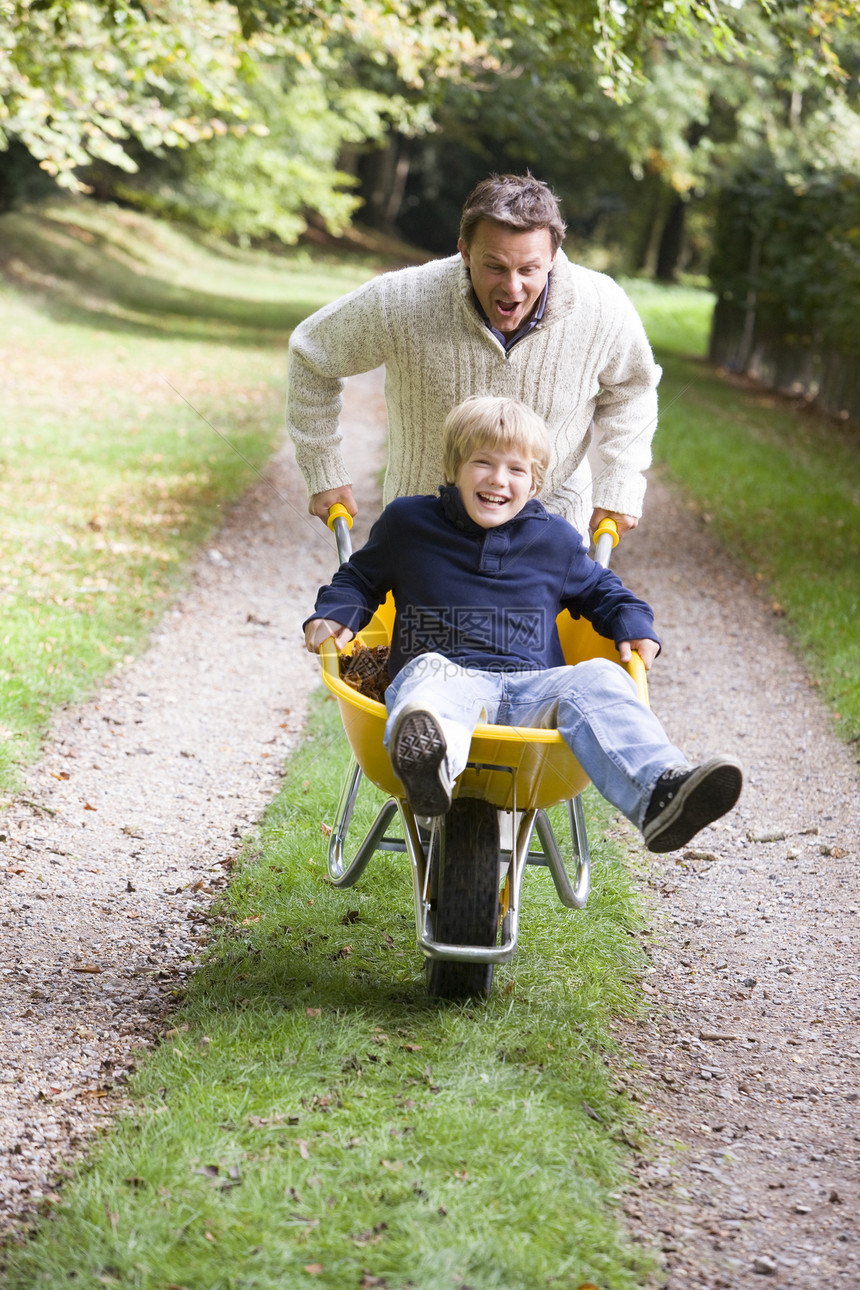 父亲和儿子在路上推着手推车大自然叶子工具成年孩子们美化树叶男人爸爸们爸爸