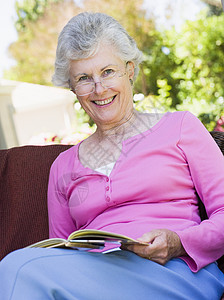 坐在户外的高级妇女坐在椅子上阅读一本书女士微笑背景图片