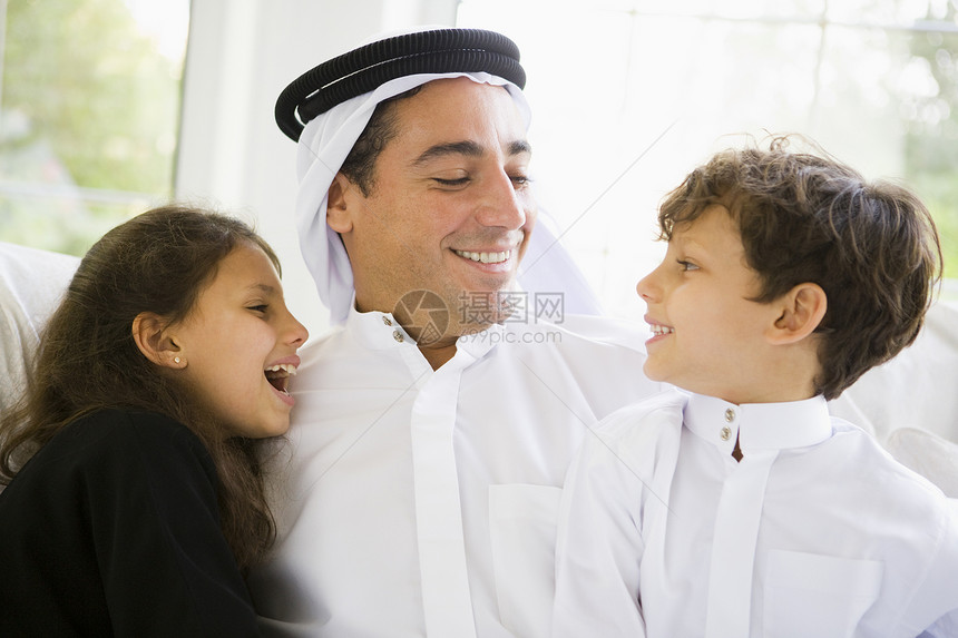 父亲和两名年幼儿童坐在客厅里微笑高关键选择性重点亲热爸爸们人种爸爸成年人感情孩子衣服女儿成人图片