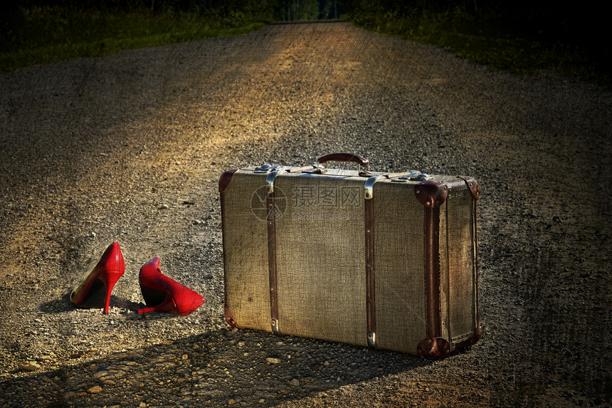 公路上留下红色鞋子的旧手提箱图片