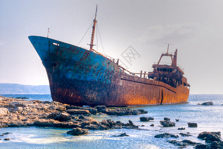 在岩石礁上搁浅的老沉船货轮悬崖导航蓝色损害海滩金属腐蚀海岸支撑背景图片
