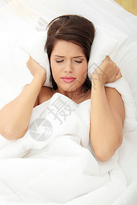 女性用枕头闭上耳朵卧室挫折沮丧女士黑发疾病就寝噪音压力苏醒床高清图片素材