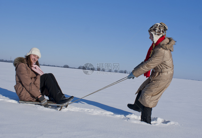 两个快乐的姐妹在冬天滑雪平底享受天气女孩们行动游戏青春期雪橇下雪帽子图片