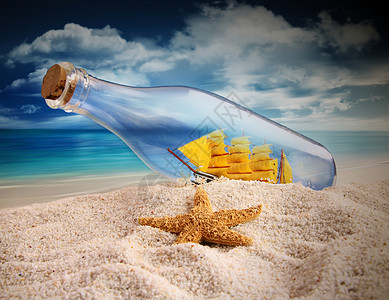 瓶子里船装在船瓶子里 躺在沙沙中支撑海洋玻璃秘密天堂海盗纪念品蓝色海星土地背景