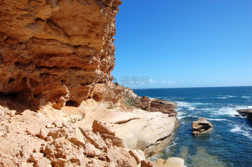 红岩与海洋海岸蓝色波浪蓝天海浪悬崖红色支撑洞穴岩石图片