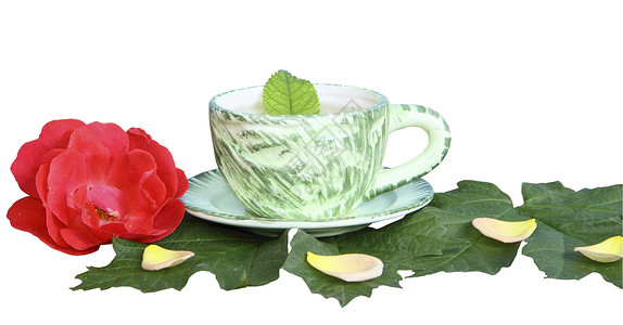 白色背景的绿页上茶杯中的茶红色飞碟绿色花瓣床单黄色陶瓷玫瑰商品背景图片