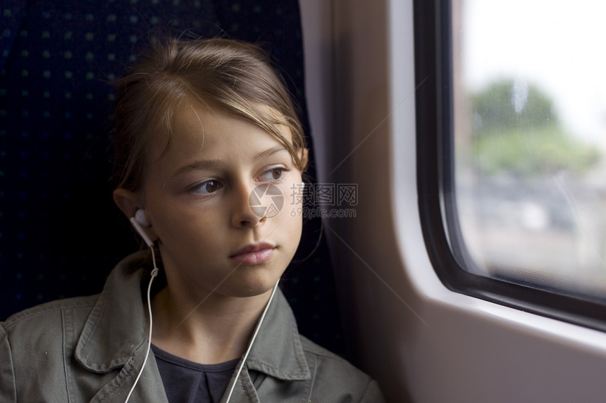 有耳机的女孩在火车或公共汽车上向窗外看图片
