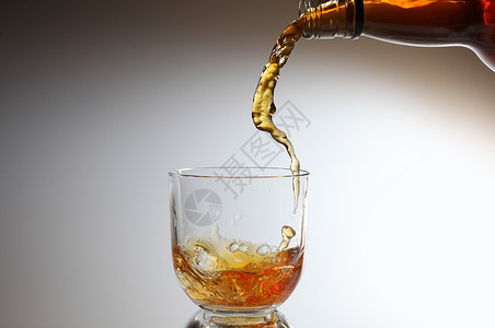 威士忌倒在玻璃杯里玻璃飞溅液体流动瓶子背景图片