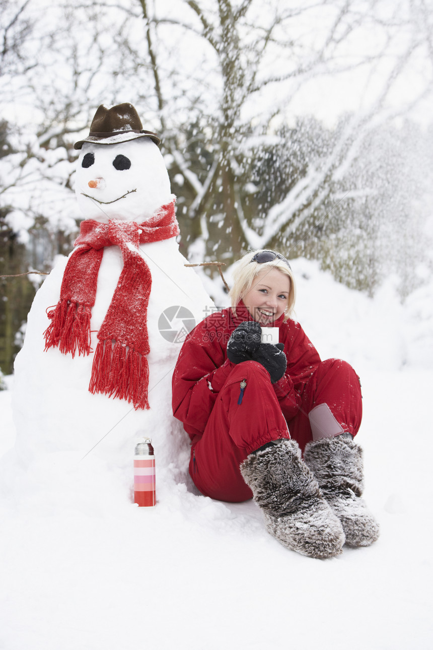 女孩在雪人旁边 带着火瓶和热饮图片