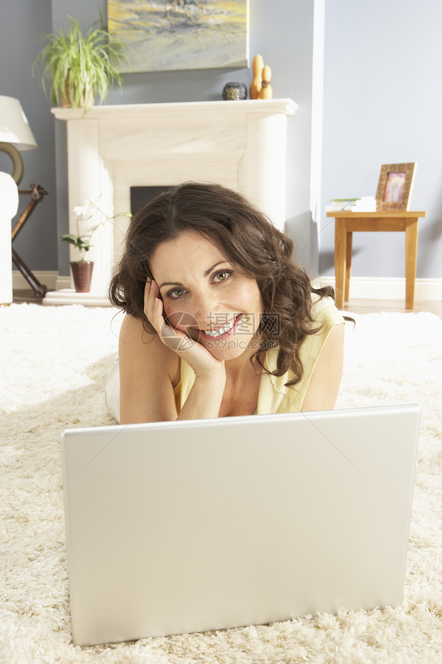 妇女在家里使用膝上型电脑轻松地躺在Rug上微笑闲暇长度互联网冲浪娱乐成人客厅笔记本地毯图片