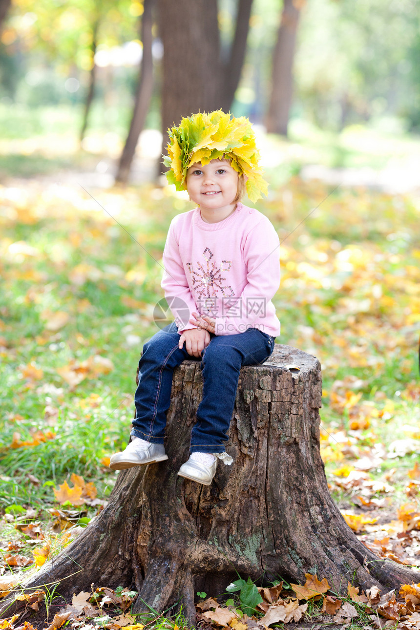 美丽的小姑娘 坐在石板上 坐着一朵满是青梅树叶的花圈里乐趣喜悦树桩微笑季节公园橙子童年幸福压痛图片