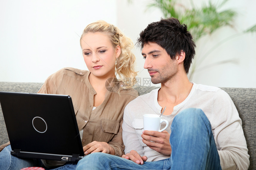 一对夫妇用咖啡和笔记本电脑在沙发上放松图片