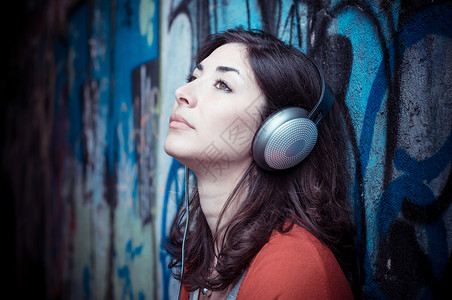 听音乐的漂亮时装女人城市音乐玩家说唱涂鸦耳机短裤女性衬衫街道背景图片