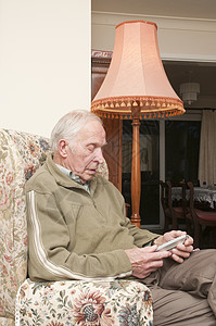 老年人用电视遥控器坐在扶手椅上背景图片