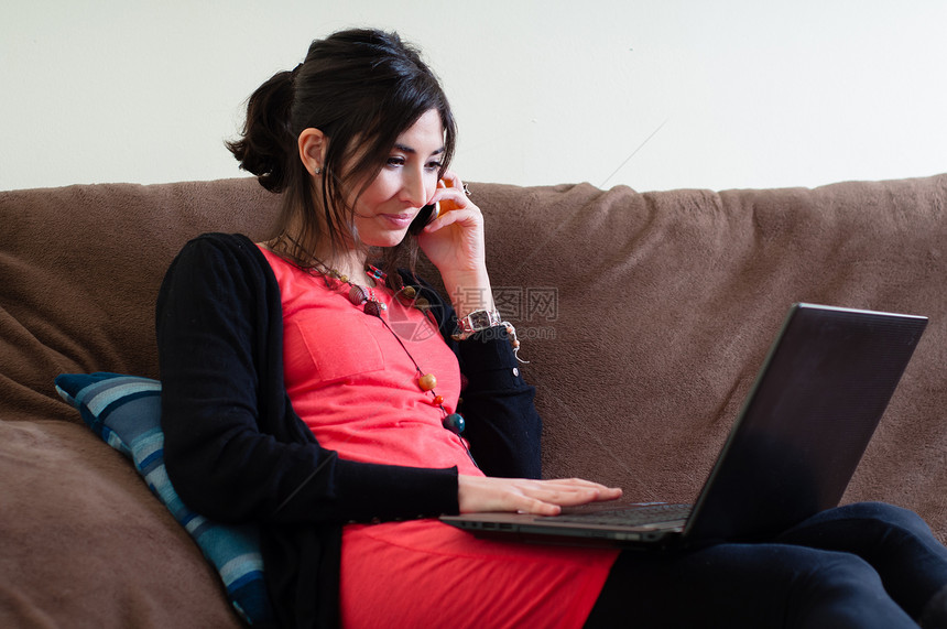 妇女在家里使用笔记本沙发女士房间电话黑发闲暇女孩长椅技术呼唤图片