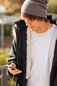 英俊的年轻人在户外咨询电话男人耳机微笑公园夹克背景图片