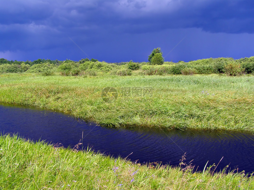 暴风雨前绿地上的小河图片