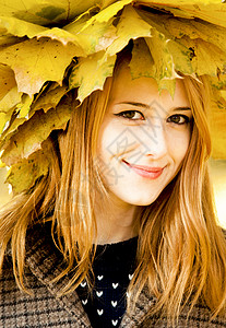顶着树叶的女孩在秋天的树叶上微笑着快乐的女孩橙子叶子少年头发公园后代毛衣青少年女性感恩背景