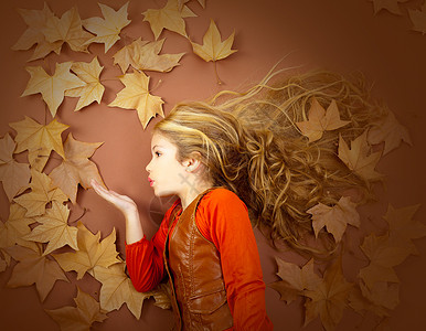 叶子上女孩秋天女孩在干叶上吹着风的双唇嘴唇地面孩子季节童年美丽叶子头发金发树叶背景