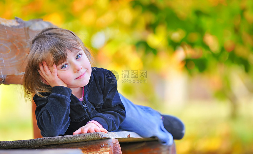小女孩坐在公园的长椅上女孩树木童年孩子喜悦乐趣金发裙子青年女性图片