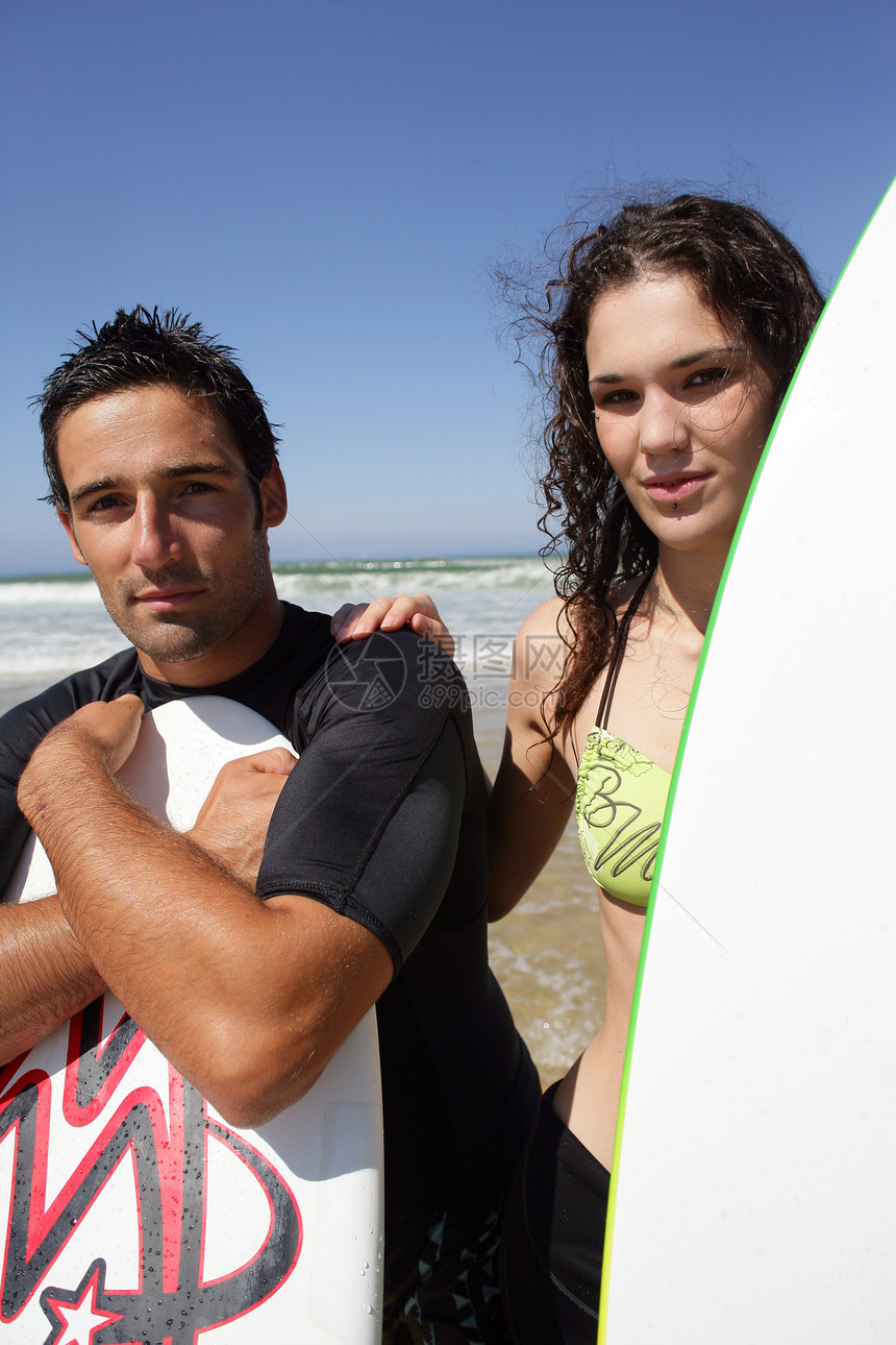 年轻冲浪情侣站在海滩上 带着他们的冲浪板图片