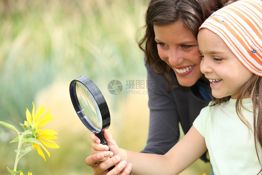 母亲和女儿用放大镜检查一朵花的鲜花图片