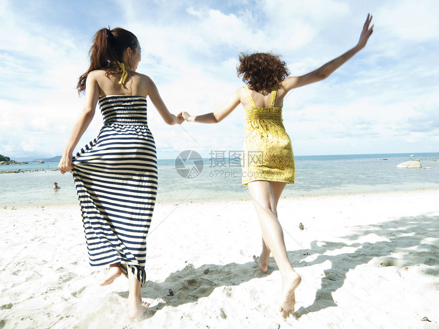 妇女一起在蓝天空背景下海边沙滩上奔跑运动海滨夫妻闲暇海洋热带假期天空恋人女士图片