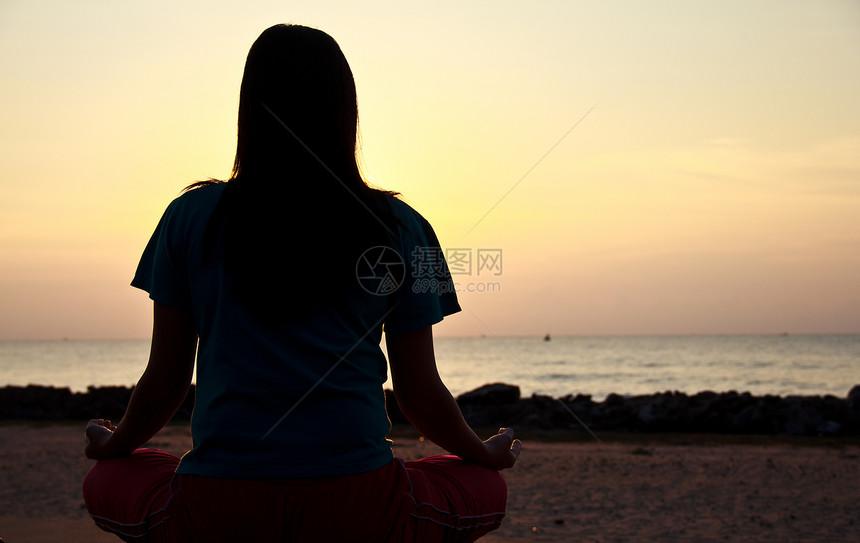 日落时在海滩冥想的女人蓝色女士活力专注头发衣服沉思女孩头脑身体图片