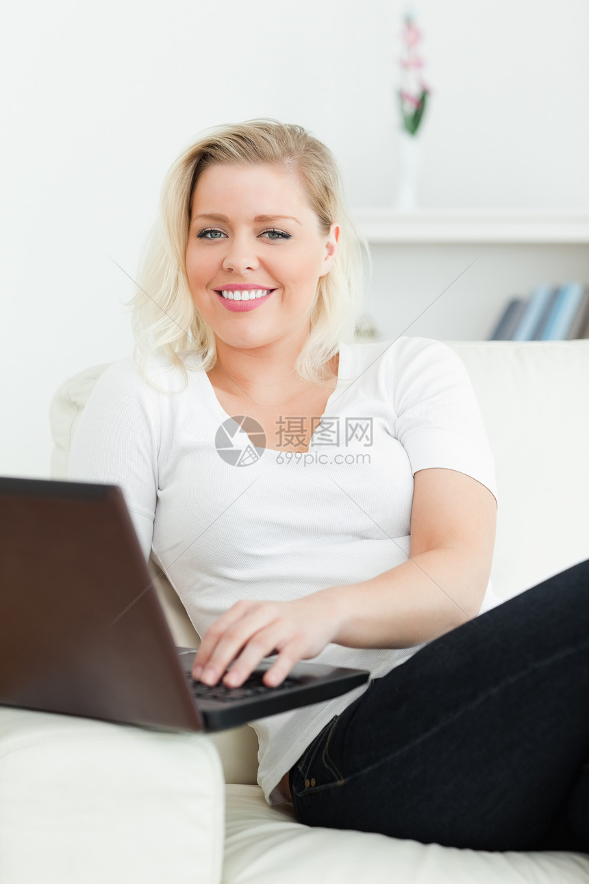妇女坐在沙发上时使用笔记本电脑白色金发快乐女性扶手休息室牛仔裤头发客厅搜索图片