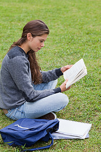 年幼严肃的女孩坐在交叉腿边看一本书背景图片