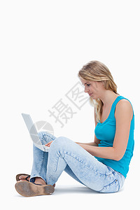 坐在地上用笔记本电脑打字的妇女的侧面视图背景图片