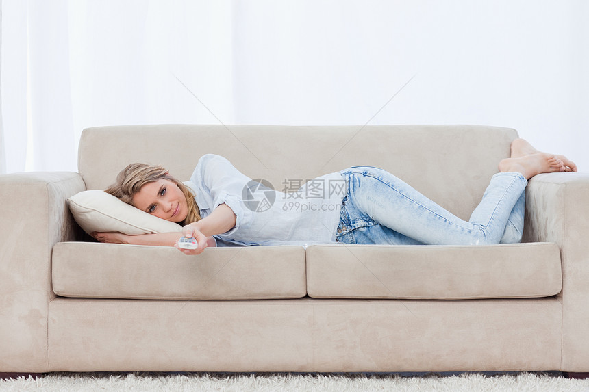 睡在沙发上休息的女士拿着电视遥控器图片
