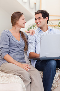 一对用笔记本电脑微笑的情侣的肖像妻子沙发网络夫妻长椅技术拥抱年轻人闲暇沟通冲浪高清图片素材