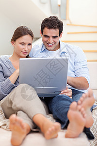 躺在沙发上时使用笔记本电脑的一对夫妇肖像技术上网微笑冲浪快乐夫妻网络妻子拥抱已婚长椅高清图片素材