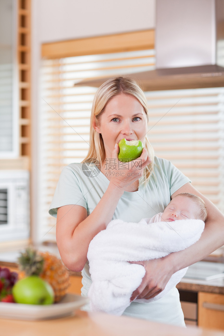 怀着一个苹果的新生儿的母亲在她的手臂上图片