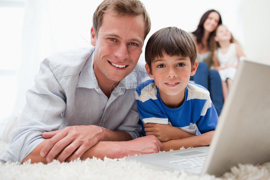 男孩和他父亲在地毯上用笔记本电脑图片