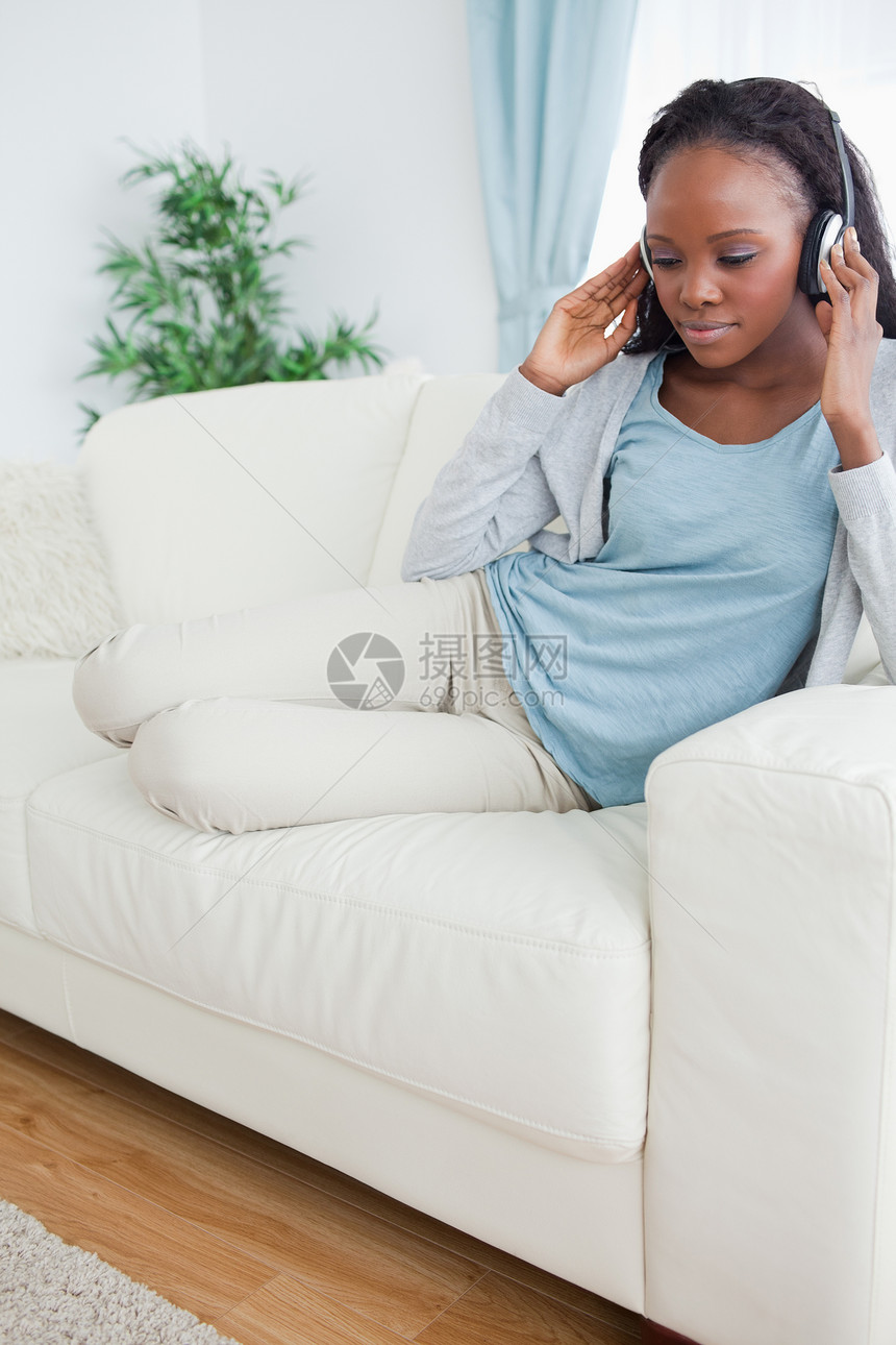 女人用音乐在沙发上放松休息快乐耳机乐趣听力说谎客厅享受长椅喜悦图片