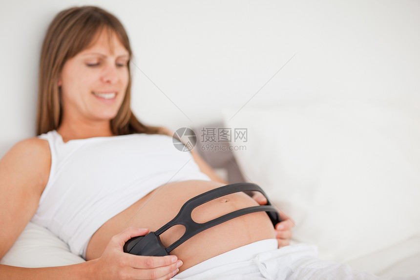 睡在床上时使用耳机的有吸引力的孕妇图片
