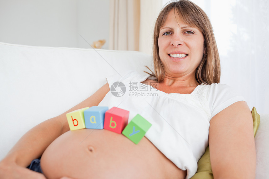 可爱的孕妇在躺着时用木木木板玩耍长椅怀孕妻子女士腹部客厅立方体沙发喜悦女孩图片