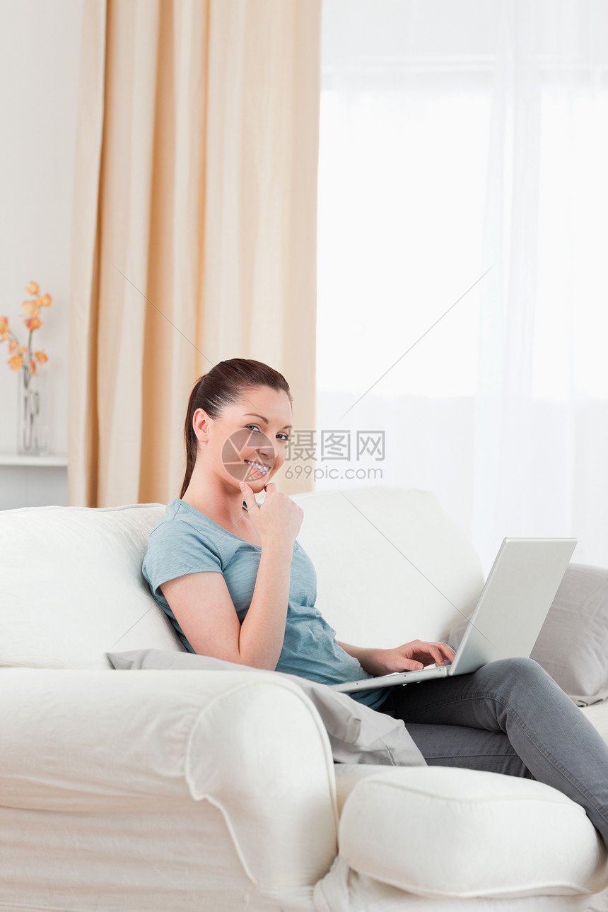 美貌美丽的女人坐在沙发上用笔记本电脑放松图片