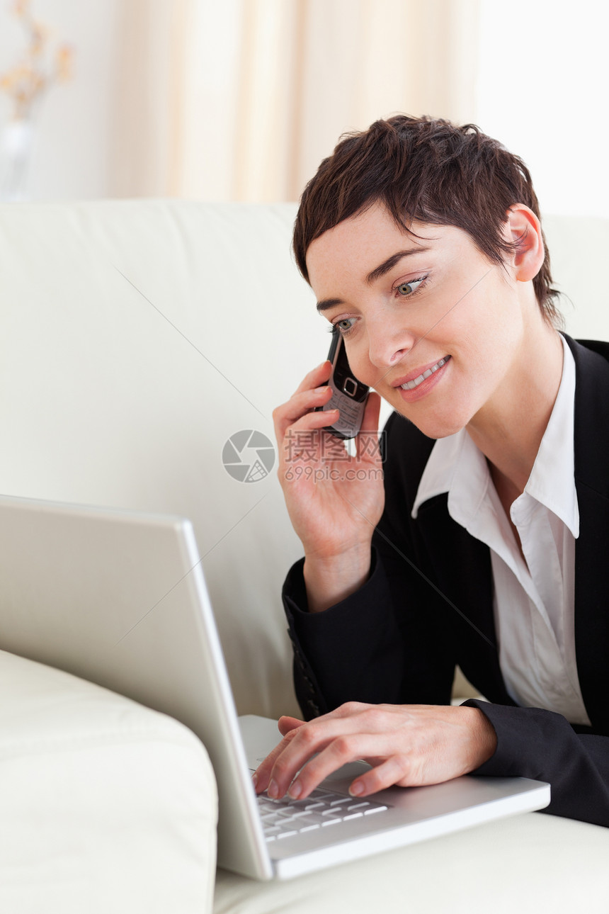 用笔记本电脑和电话躺在沙发上的女商务人士图片
