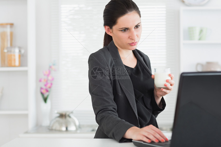 妇女一边看笔记本电脑 一边拿着牛奶杯图片