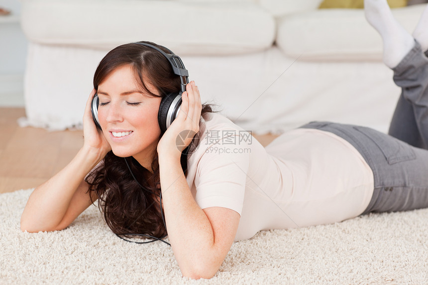 在地毯上躺着时使用耳机的深色黑发女人图片