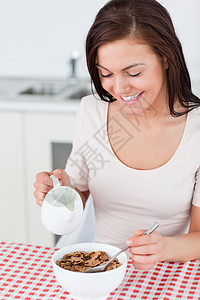 麦片碗里女孩一个微笑的黑发美女在麦片里倒牛奶的肖像背景