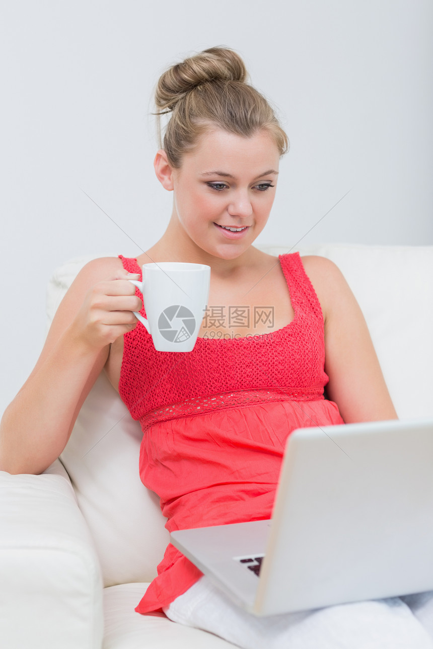 妇女使用笔记本电脑时喝咖啡长椅家庭浅色快乐金发女郎客厅金发杯子头发饮料图片