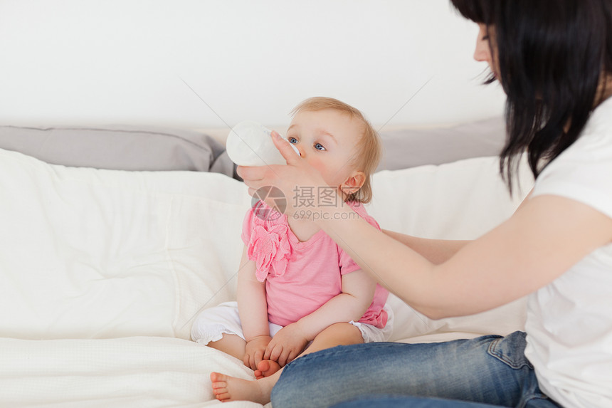 美丽的黑褐色女性在床上用瓶子喂婴儿图片